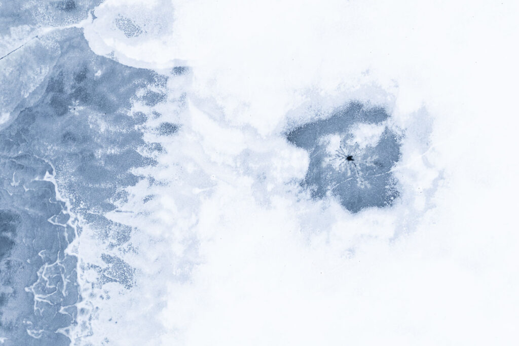 Abstract frozen water surface with cracks, snow textures and a dark spot in ice