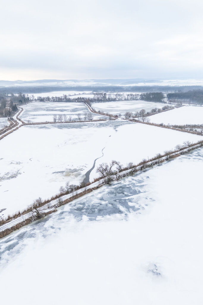 Aerial view of frozen reservoir in winter with snow-covered paths and trees
